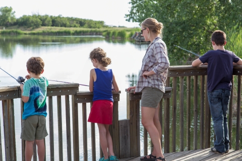 An adult watches a young boy and girl fishing from a dock.