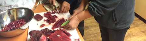 Red caribou meat being cut into slices and cubes on a kitchen table