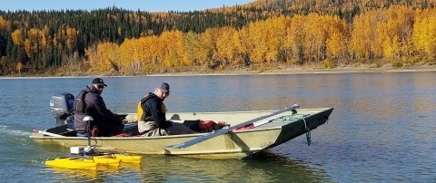 Two men in a small motorboat assessing water quality on a river in fall