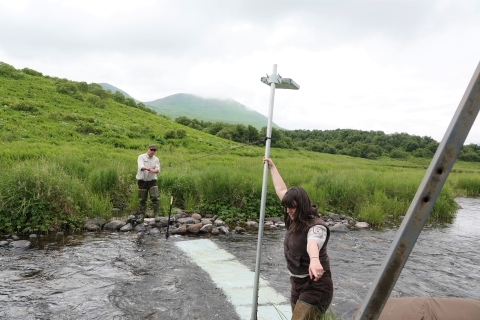 Two people in USFWS uniforms erect a light over a stream survey sight