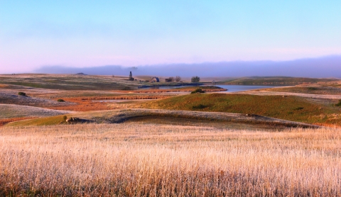 A prairie landscape with an old barn, a wetland, and fall-colored rolling prairie hills in Logan County, North Dakota