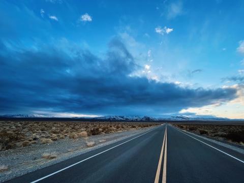 An empty road heads into the distance while dark, ominous clouds fill the sky above