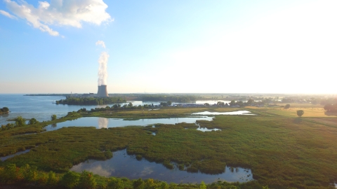 Aerial view looking down to a green marsh next to Lake Erie with large nuclear power cooling towers in the background