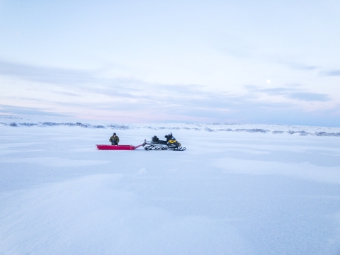 a snowmobile with plastic sled attached sits on the smooth white ice of a frozen lake.