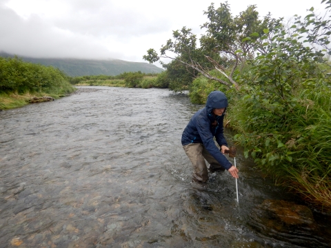 person in rain gear taking a measurement in a stream