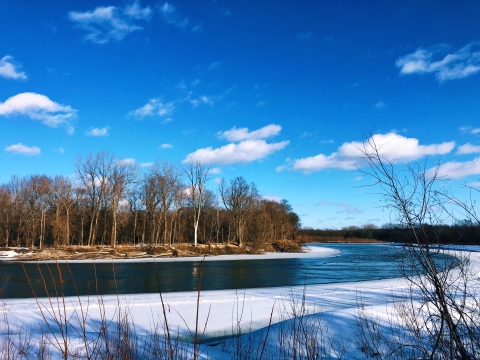 Open river in winter with snow on ground and blue bird sky.