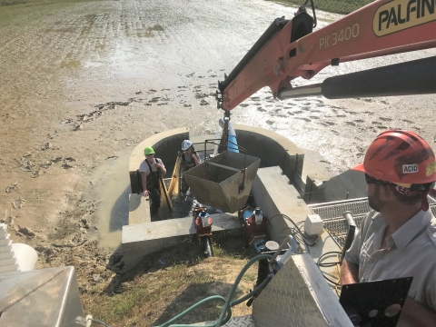 USFWS biologist lowers large bucket using a crane into a newly constructed test kettle in order to move fish out of the pond.
