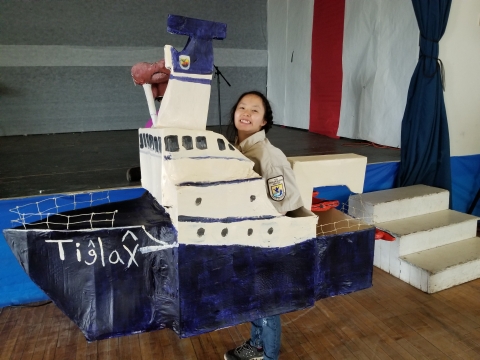 Child wears a replica of a blue and white ship as if she's steering it.