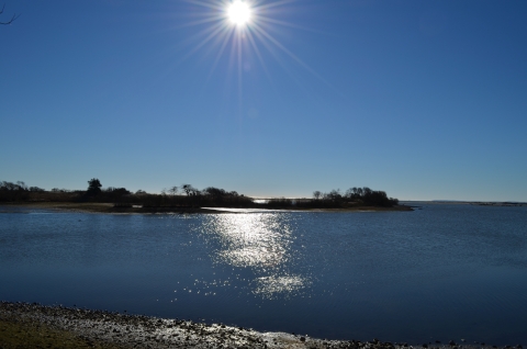 The sun in a crystal clear blue shy over a piece of land jutting into water