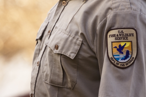 A close up of a U.S. Fish and Wildlife Service staff wearing the Service uniform's beige shirt with the shield patch on the shoulder. 