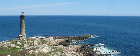 A tall, slender stone lighthouse on a rocky coast of the deep blue ocean