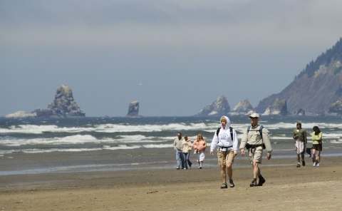 Three groups walking on the beach on the coast with mountains and eroding rock in the surf.