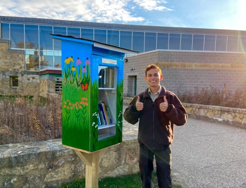 Ranger Logan Sauer stands next to the new tiny library outside the visitor center. The library is painted with native flowers.