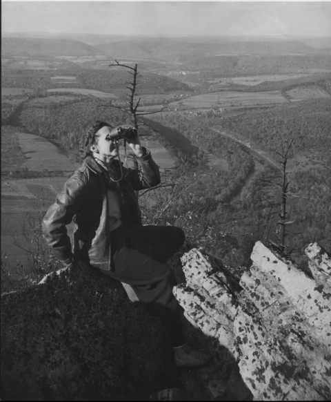 woman sitting on top of rock overlooking edge thru binnoculars