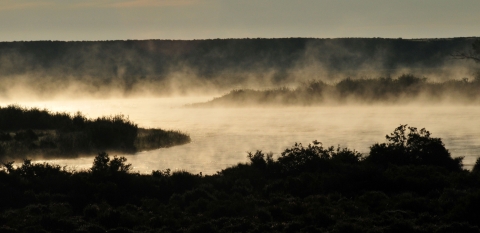 Mist rises off a river at sunrise.
