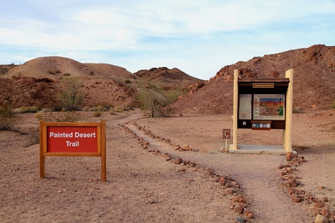 A sign indicating the Painted Desert Trail stands next to a trail running through the desert hills.