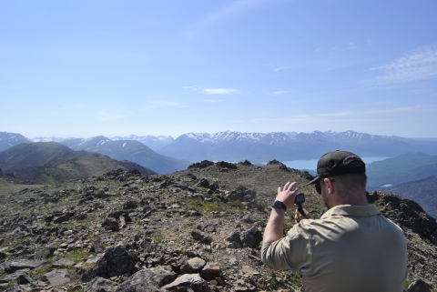 A person holding a camera taking video on a mountain top.