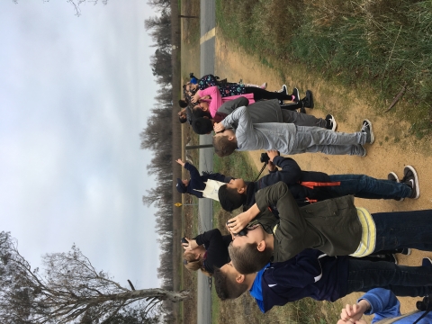 group of about 10 kids looking at something with binoculars. ranger pointing toward sky