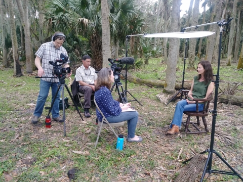 man recording with video of woman interviewing another woman outdoors