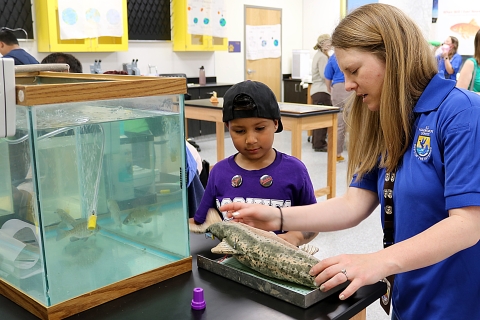 A woman and a boy measure a replica fish in front of an aquarium