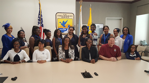 FWS employees and Zeta Phi Beta Sorority sitting and stand with official Service logo and flags in the background. 