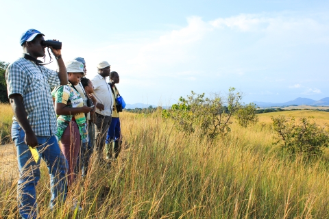 Students look out over an African grassland, the one closest to the camera through binoculars