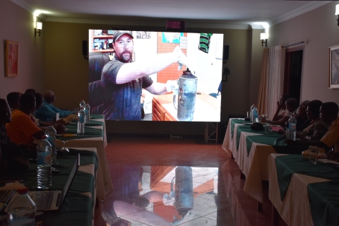 class watches man on video screen with what looks like metal jug