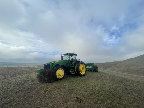 A tractor is in the middle of the frame with bare ground and a cloudy sky 