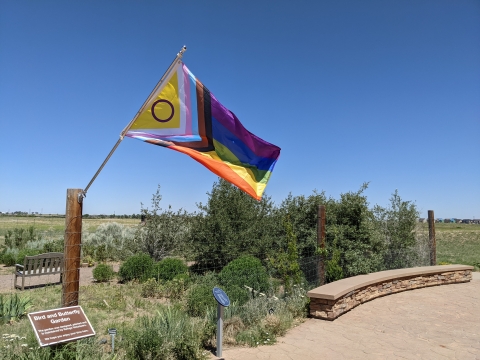 colorful flag flies over sign that reads, Bird and Butterfly Garden above smaller text