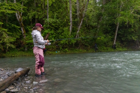 Fisheries intern, Hannah Ferwerda, wading in water and reeling a fishing rod as she samples river for fish.