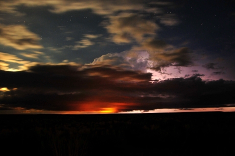 Sunset, stars, and storm clouds converge over a silhouetted landscape
