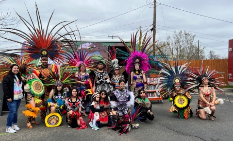 People in tradition dress are posed for a picture in a group. The outfits are very colorful and they are wearing feathered head-dresses. 