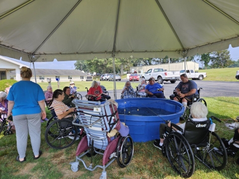 Elderly people fishing out of blue stock tub under a tent