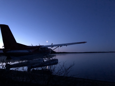Airplane sitting on water at night with the moon in the background