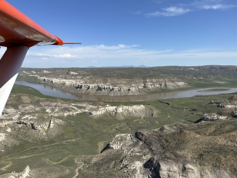 view of an airplane wing over the landscape of a river 
