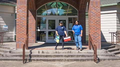 Two Service interns posing with fishing gear in front of a library. 