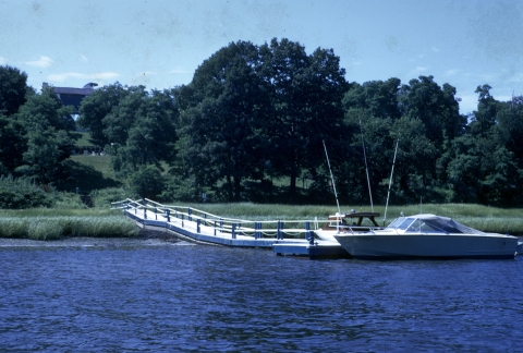 A small motorboat pulls up alongside the end of a dock.