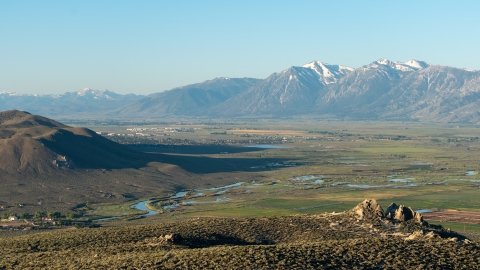 A view looking into Carson Valley during sunrise. Tall mountains are off in the distance with a valley filled with sagebrush below. A river cuts through the valley.