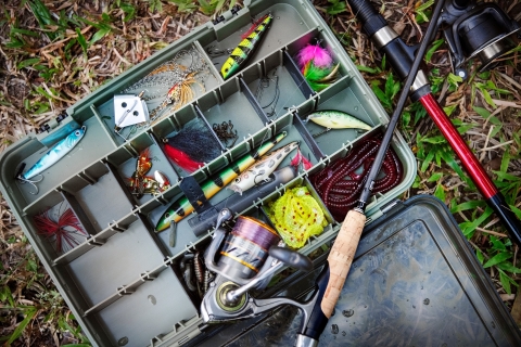An open tackle box full of colorful fishing lures, hooks, and a fishing rod. 