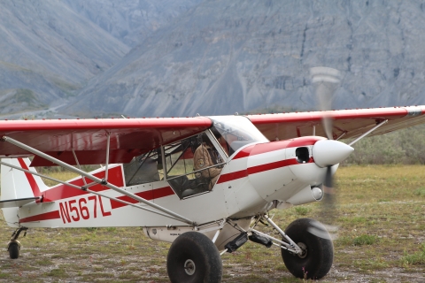 Close up of a Refuge Federal Wildlife Officer in a Top Cub bush plane as he prepares for take off from a dirt airstrip with mountains covering the background just out of focus. 