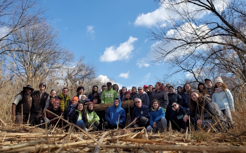 a large group of people stand together in nature with a bundle of phragmites