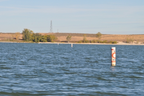 A line of separated buoys out on a lake with text that reads “No Wake” and an open orange circle in between.