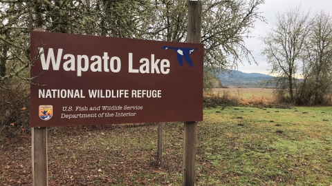 Picture of the Wapato Lake National Wildlife Refuge sign. The refuge is in the background.