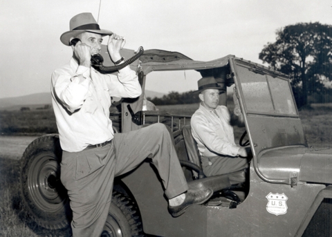 Two men in vehicle, one on a portable radio