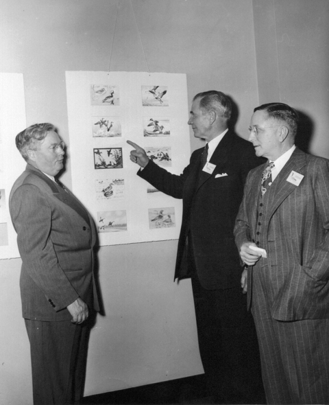 Three men standing around duck stamp entires on wall