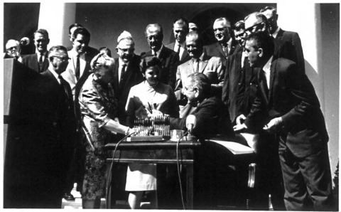 Crowd of people around President Johnson at a table