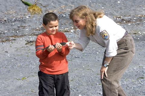A woman in a USFWS uniform bends over to talk with a child holding a fish.