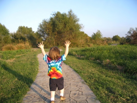 a child runs on a paved trail with its hands in the air