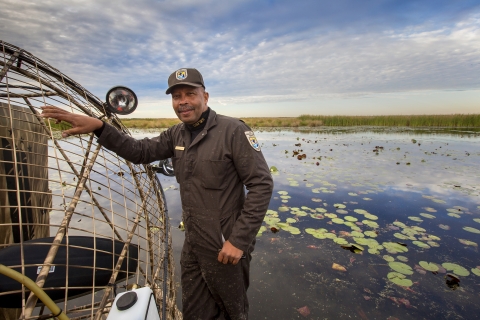 A U.S. Fish and Wildlife Service employee in uniform on an airboat in the marsh