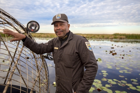 A U.S. Fish and Wildlife Service employee in uniform leaning against an airboat with a marsh in the background